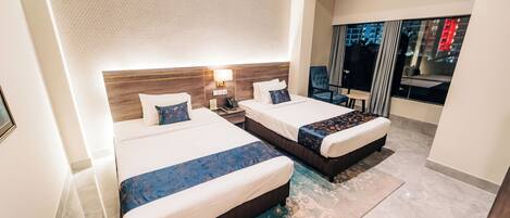 A hotel room with two beds, a large window with a view of the city, a modern headboard, and a small table.