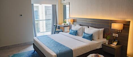 A hotel room with a large bed, bedside tables, a desk, a chair, and a view of the outside.