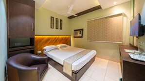 A hotel room with a bed, a desk, a chair, a television, and a ceiling fan. - Hotel Dolphin Puri (Puri)