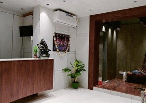 A reception area with a wooden reception desk, a potted plant, a wall-mounted air conditioner, and a television. - Hotel Dolphin Puri (Puri)