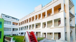A modern multi-story building with a central staircase and a green building to the left. - Hotel Dolphin Puri (Puri)