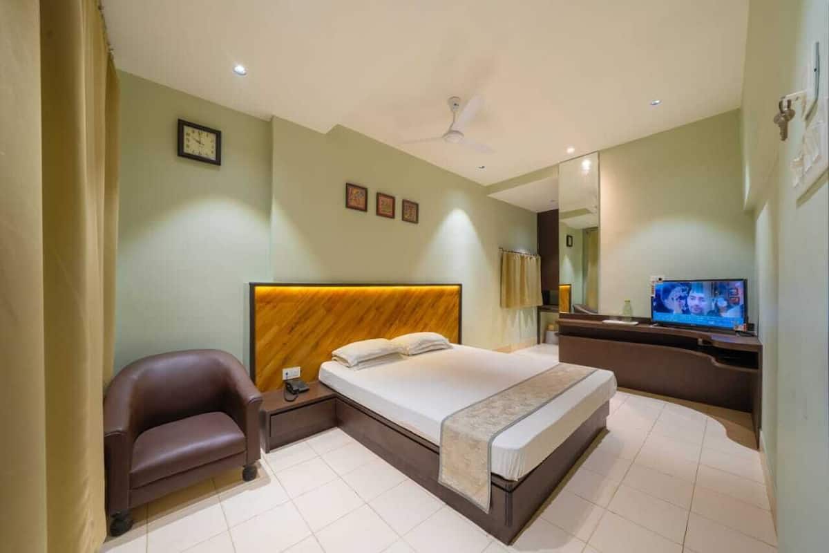 A hotel room with a bed, a chair, a desk, a television, and a ceiling fan.