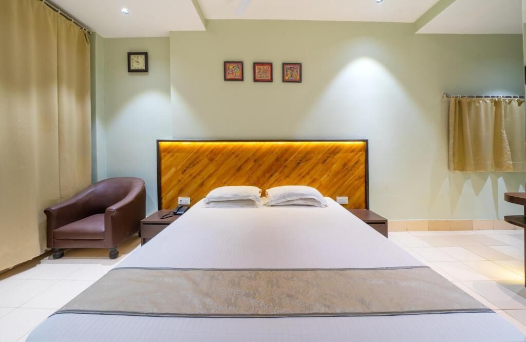 A hotel room with a large bed, a brown leather armchair, a wooden headboard, and three framed pictures on the wall.