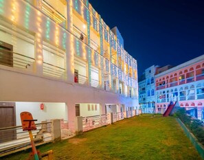 Un hôtel à plusieurs étages doté de balcons, d’une cour verdoyante et d’un terrain de jeux.