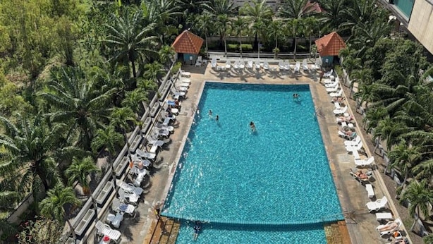 Una grande piscina rettangolare circondata da lettini e palme.