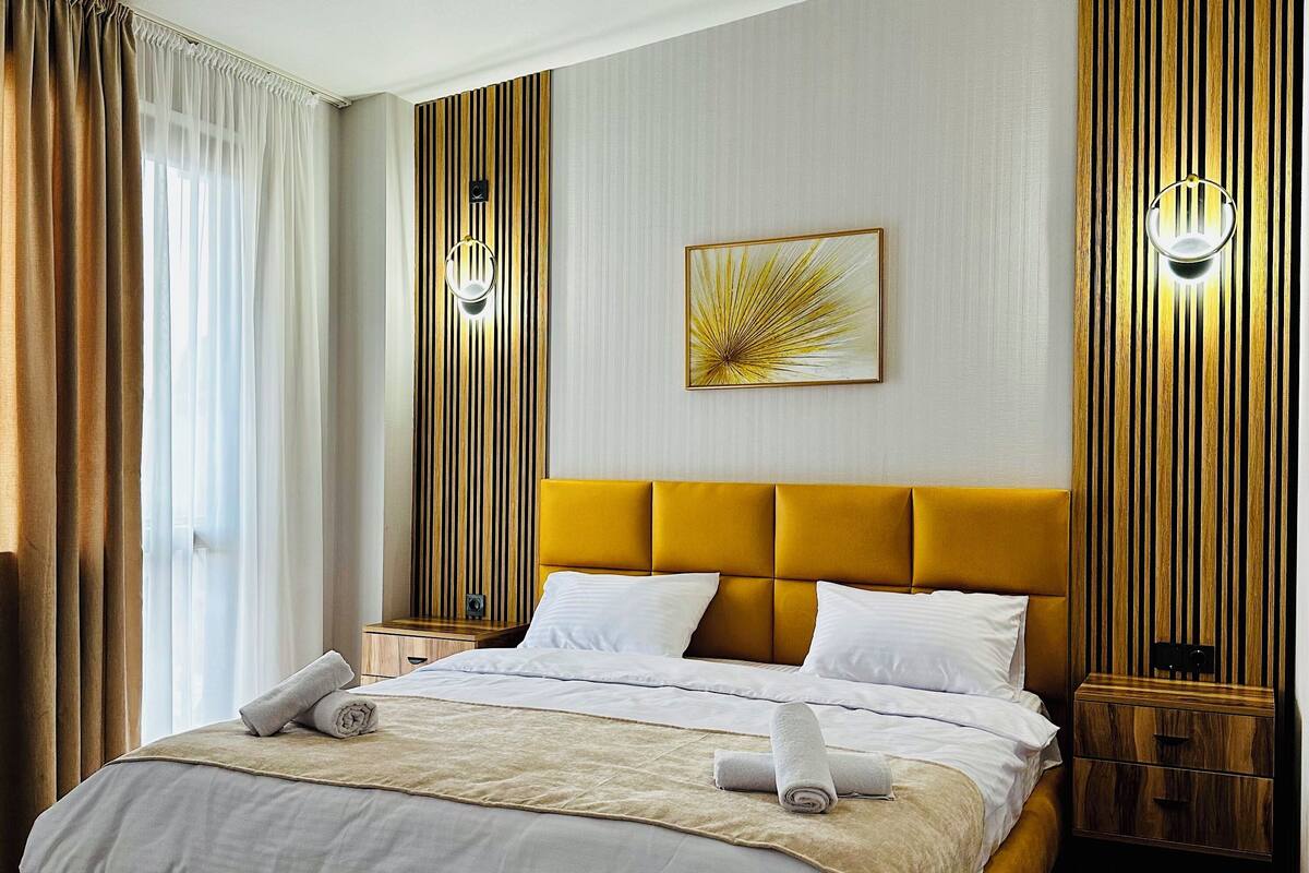 Ein modernes Hotelzimmer mit einem großen Bett, einem Holzkopfende und einem großen Fenster mit Vorhängen.