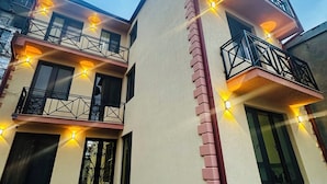 Un immeuble à deux étages doté de nombreux balcons, chacun orné d’une rambarde noire et d’une antenne parabolique. L’entrée de l’immeuble est recouverte de carreaux et le sol est constitué de carreaux décoratifs.