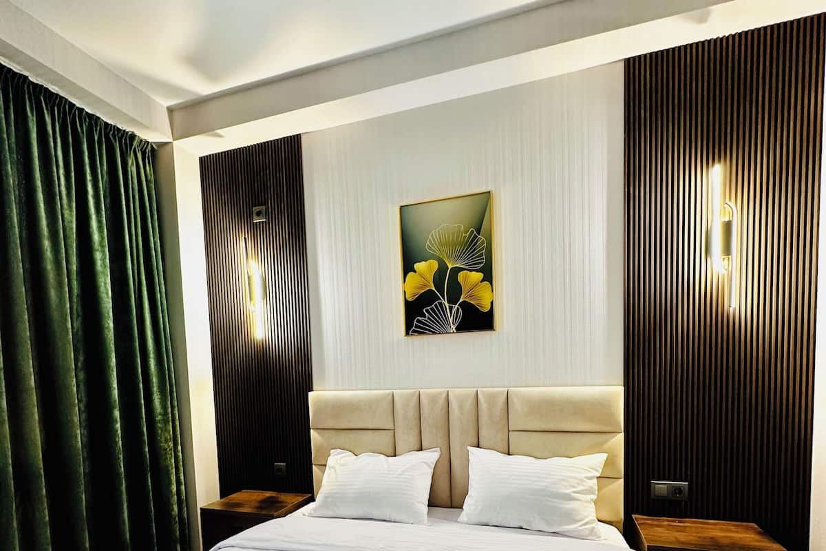 Ein Hotelzimmer mit einem großen Bett, grünen Vorhängen, einer Wandlampe und einem Wandbild.