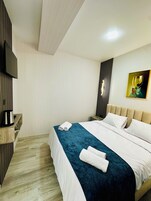 A hotel room with a bed, a flat-screen TV, a coffee maker, and a painting on the wall.