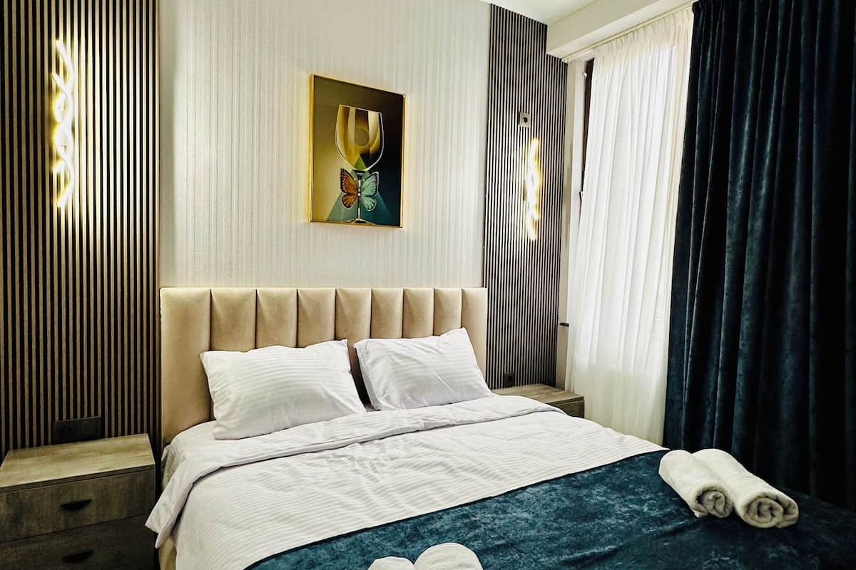 Ein Hotelzimmer mit Bett, Nachttisch, Wandbild und Vorhängen.