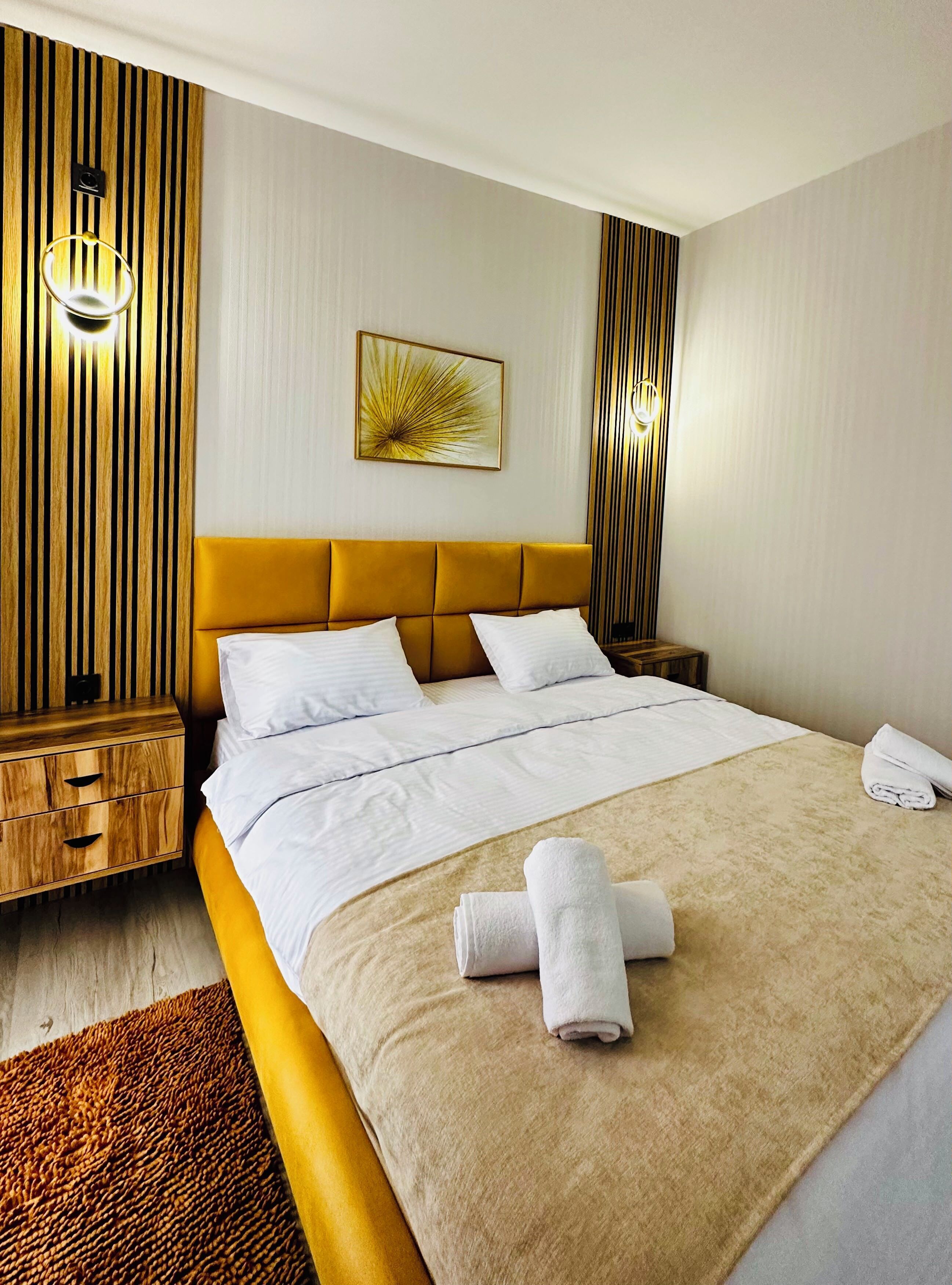 Ein Hotelzimmer mit einem großen Bett, einem Nachttisch aus Holz, einer Ablage neben dem Bett, einer Wandleuchte und einer dekorativen Wandverkleidung.