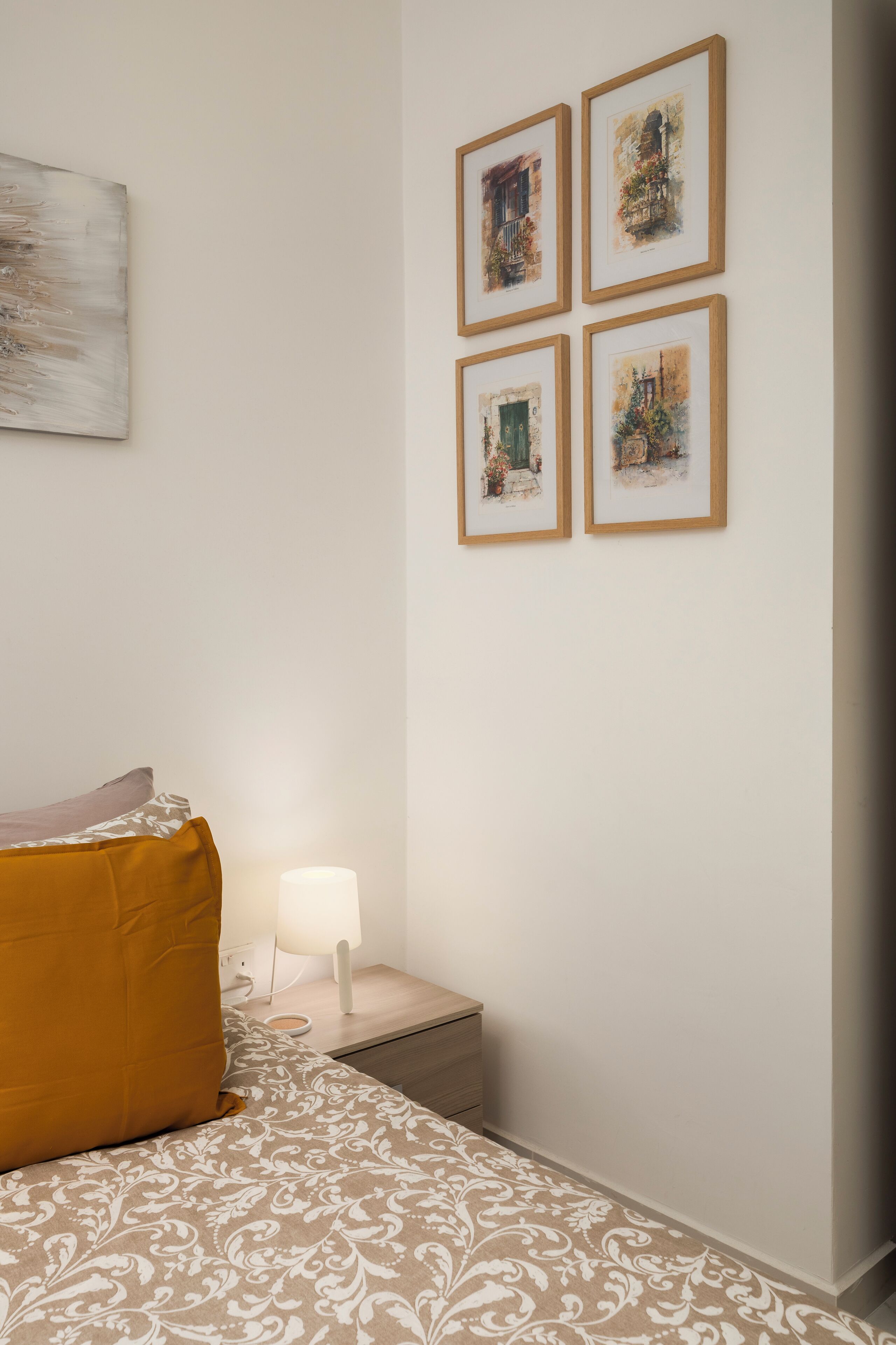 A bedroom with a bed, a nightstand, a lamp, and four framed pictures on the wall.