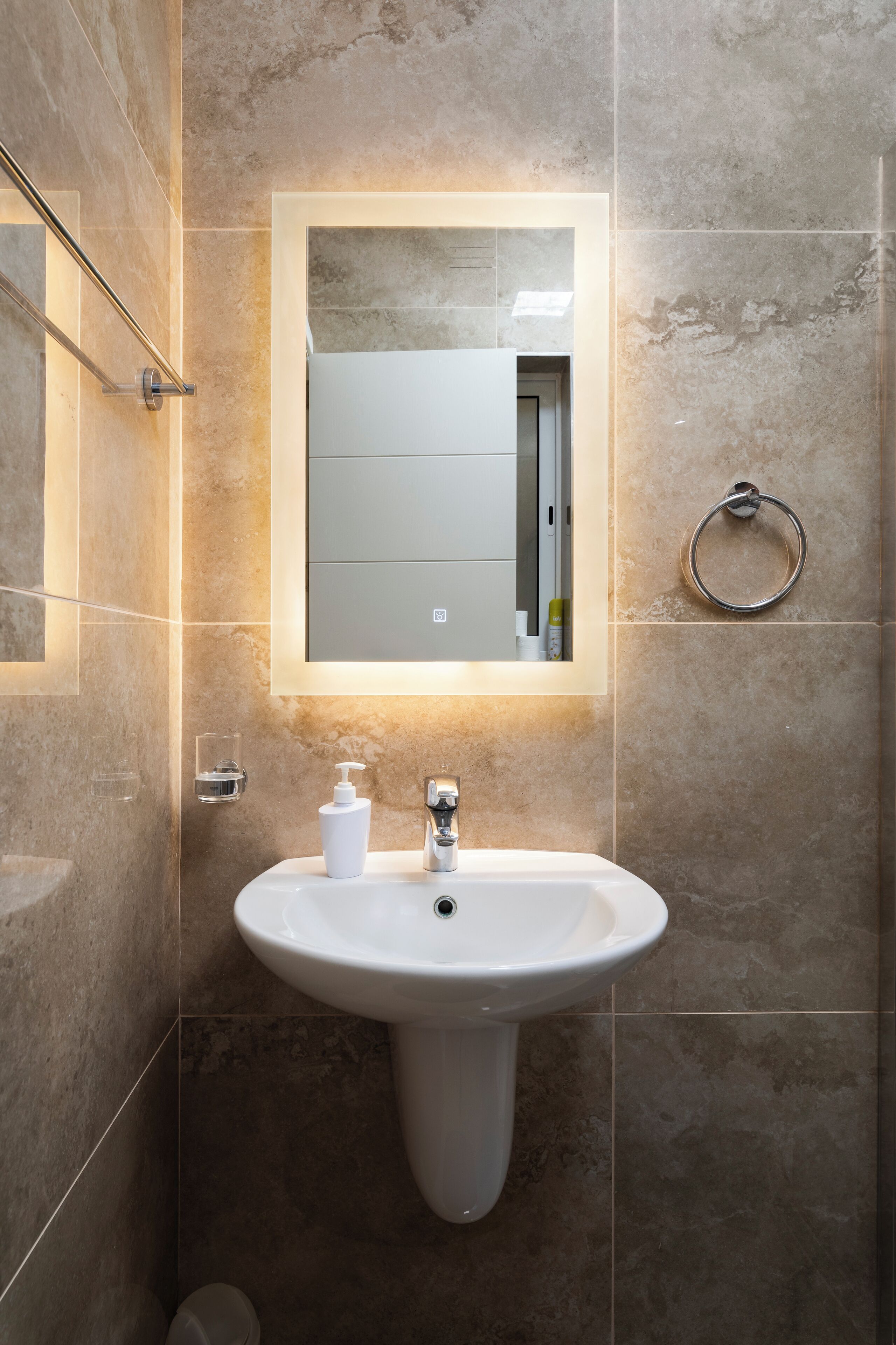 A bathroom with a pedestal sink, a mirror, and a towel ring.