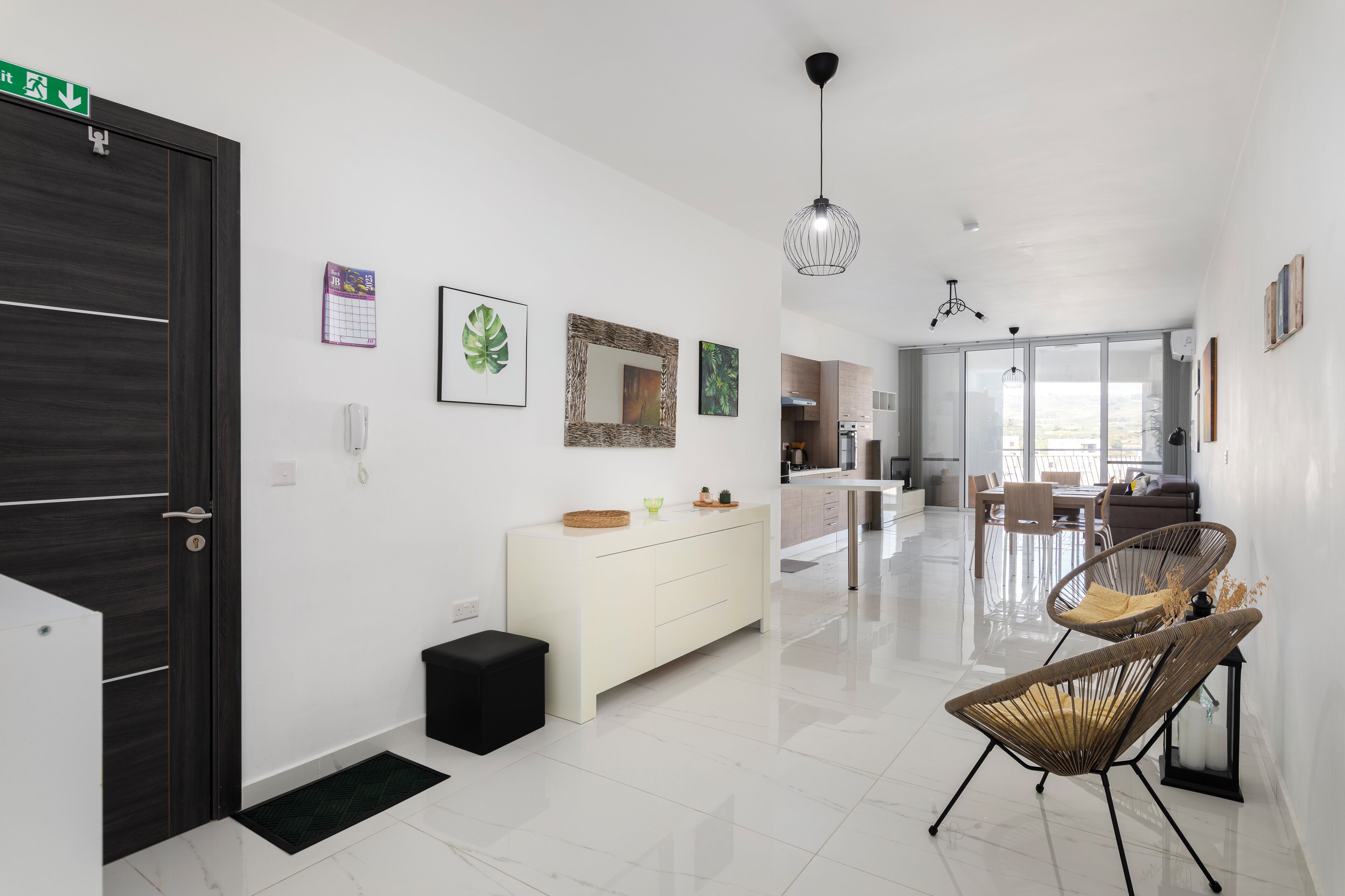 Un hall d’hôtel moderne avec un comptoir de réception blanc, une porte noire, un meuble blanc et des chaises en osier.