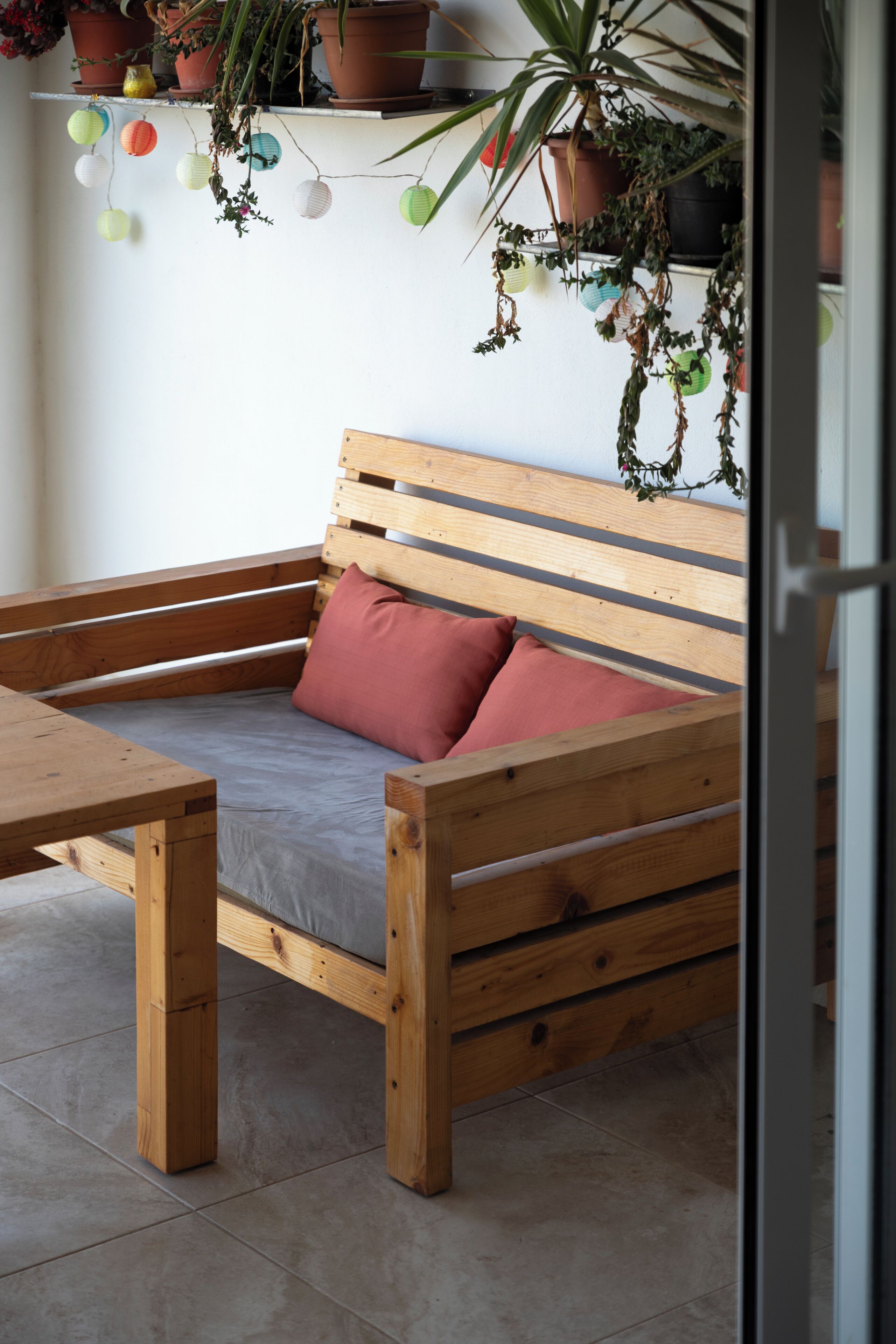 A wooden bench with cushions, a small table, and hanging plants.