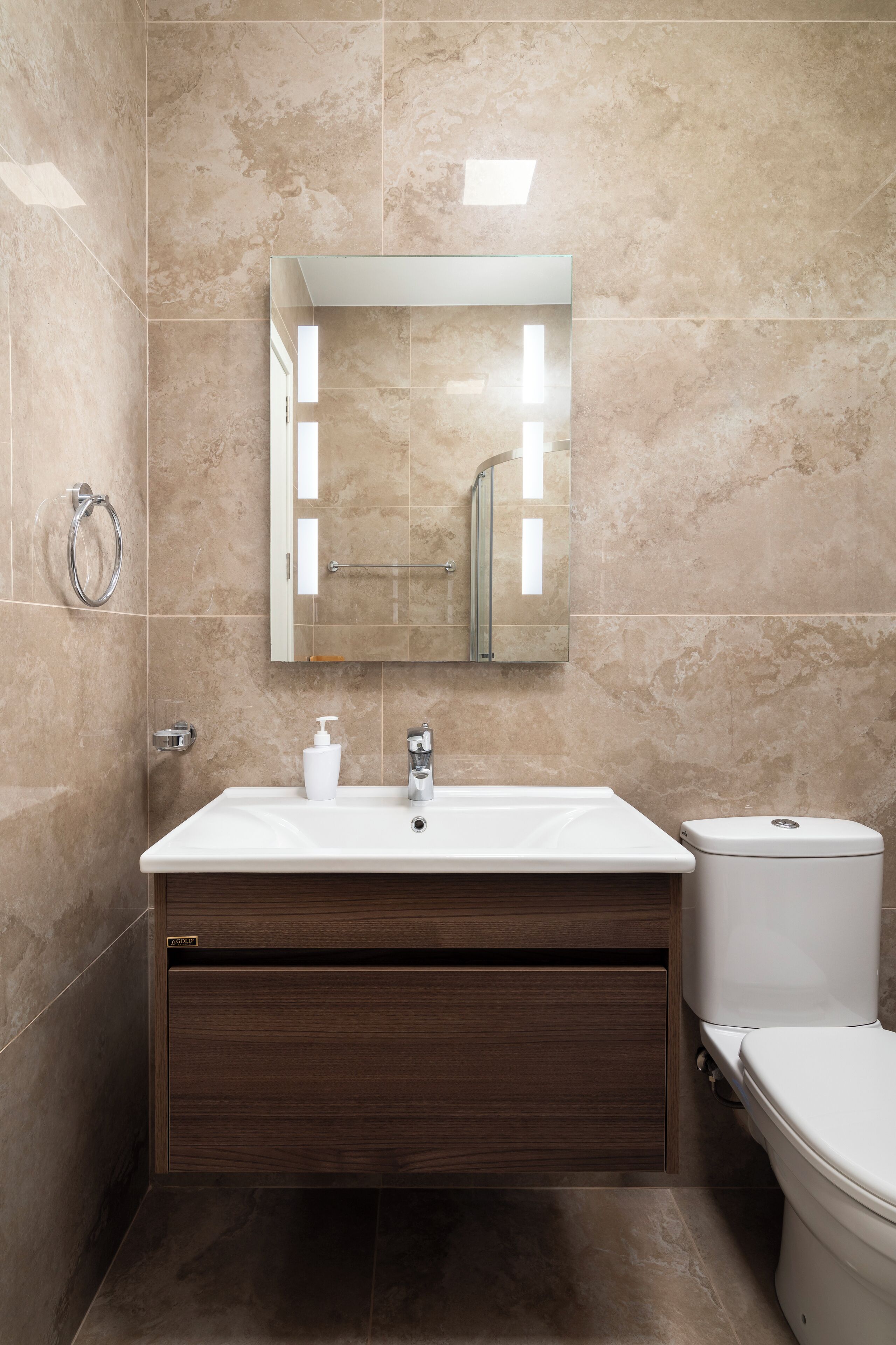 Un baño moderno con pared de mármol, un lavamanos blanco, un mueble de madera y un inodoro.