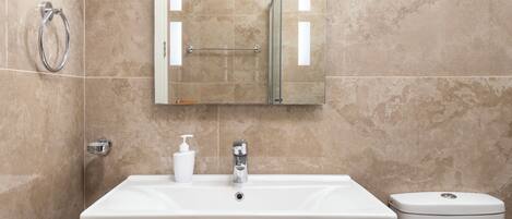 Un baño moderno con pared de mármol, un lavamanos blanco, un mueble de madera y un inodoro.