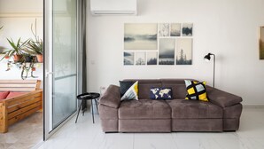 A modern living room with a brown sofa, a glass door leading to a balcony, and a wall with framed artwork. - 3BR Country Retreat with Large Terrace (Zebbug)