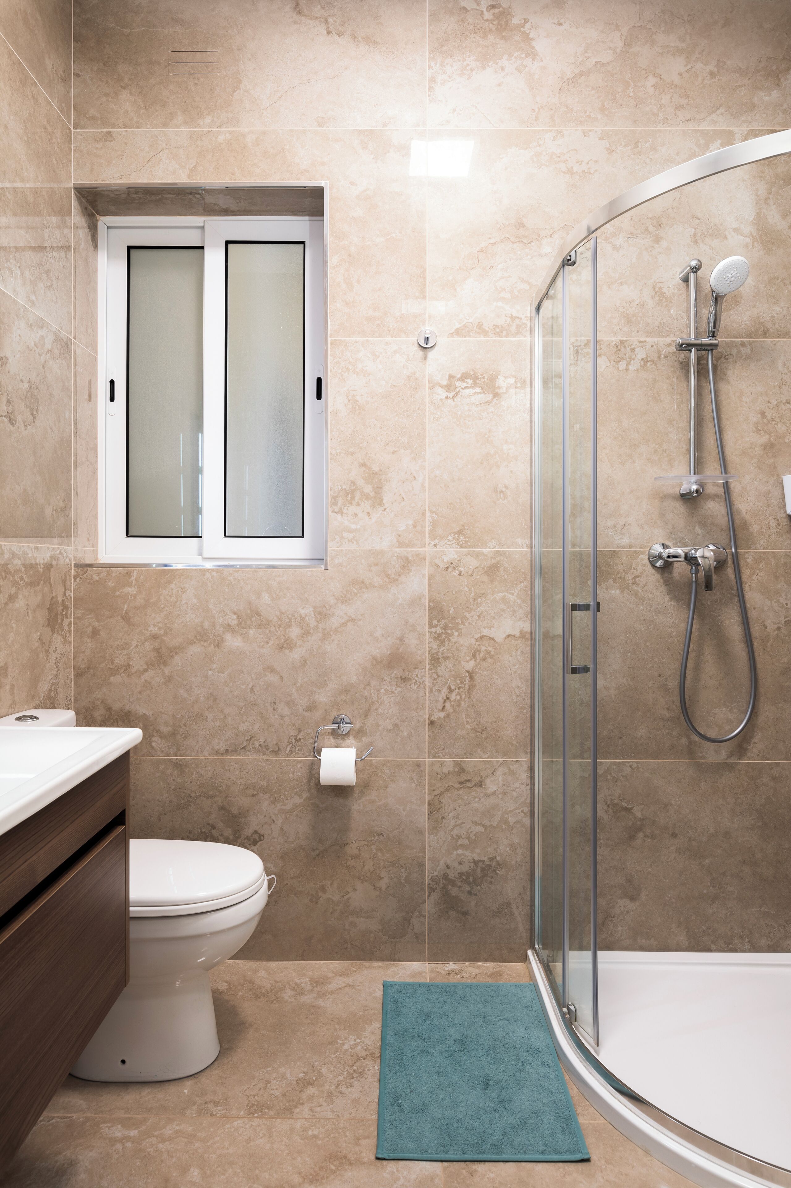 A bathroom with a toilet, a glass-enclosed shower, and a window above the toilet.