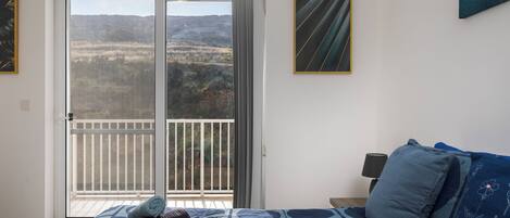 A bedroom with a bed, a nightstand, a lamp, and a view through a sliding door to an outdoor balcony.