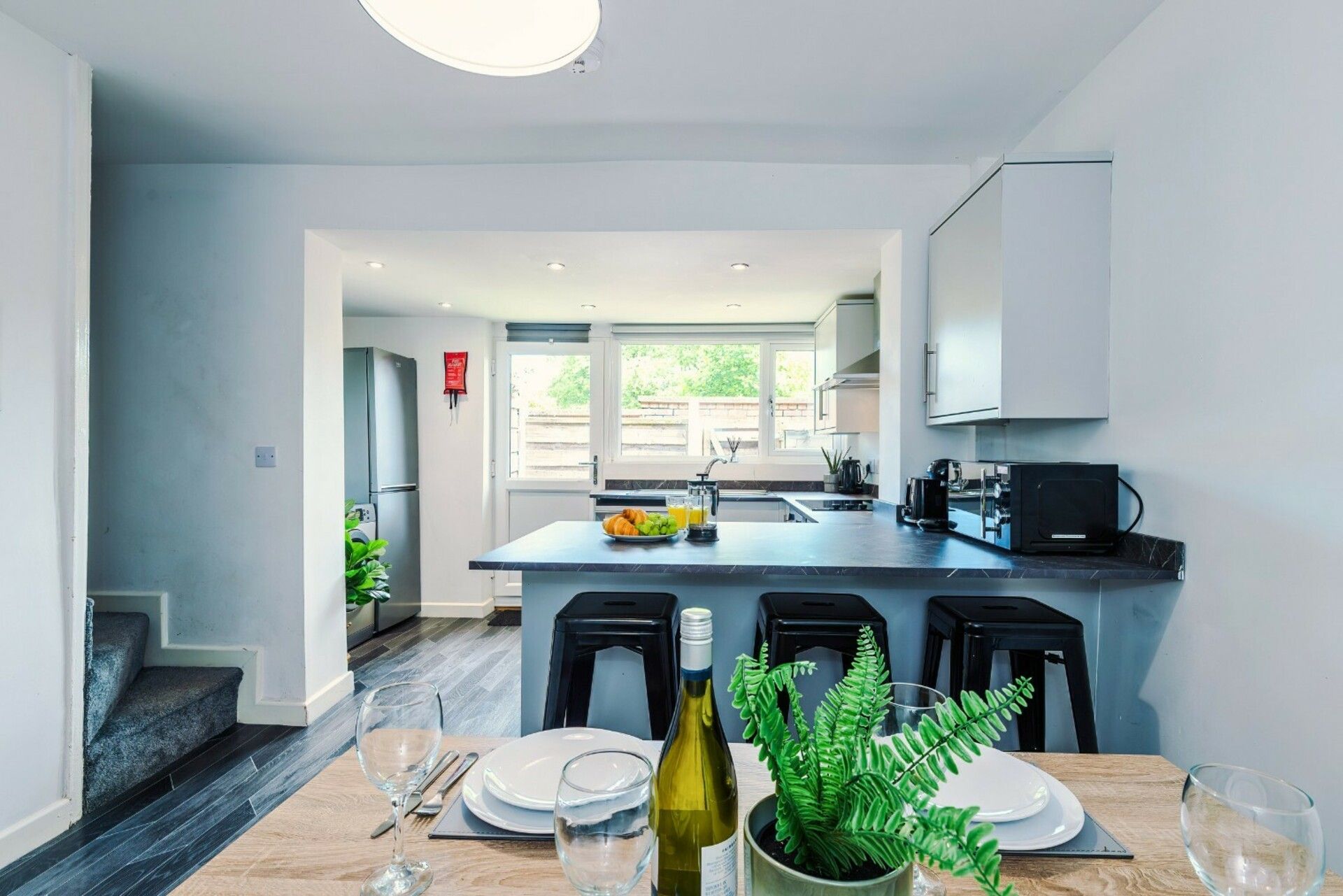 A modern kitchen with a central island, black bar stools, and a dining table set for two.