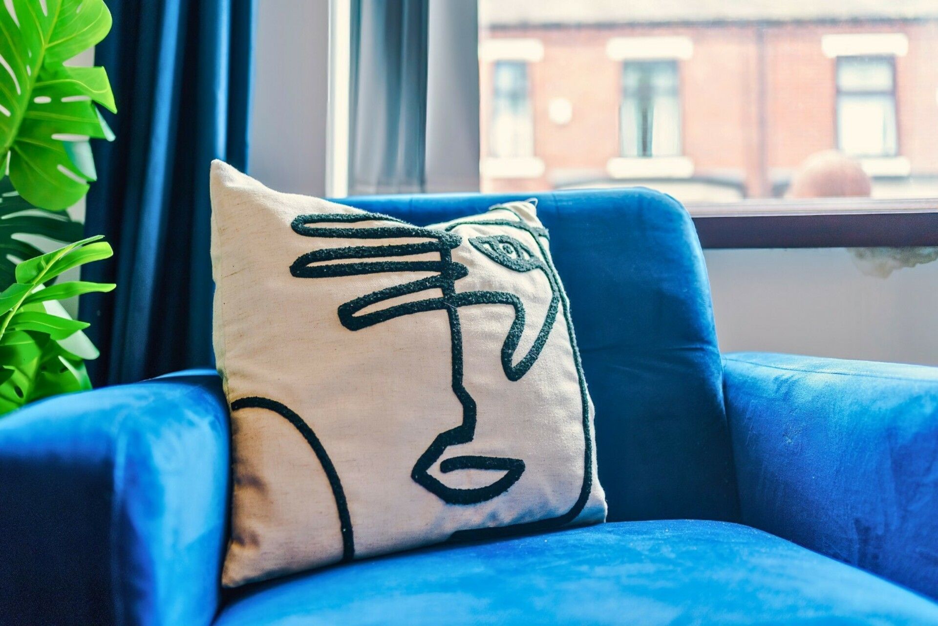 A blue armchair with a pillow featuring a black line drawing of a face.