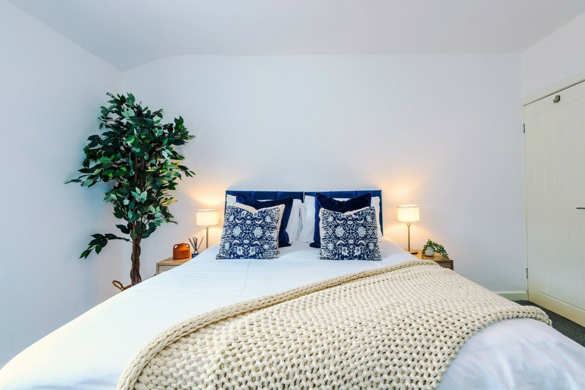 Ein Bett mit weißer Bettdecke, zwei blau gemusterten Kissen und einer beigen Strickdecke.