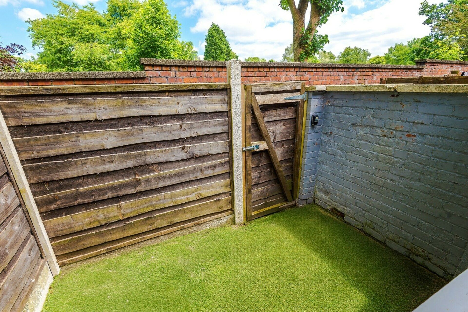 A fenced outdoor area with a wooden gate and a brick wall.