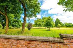 Eine Ziegelwand mit Blick auf ein grünes Feld und Bäume.
