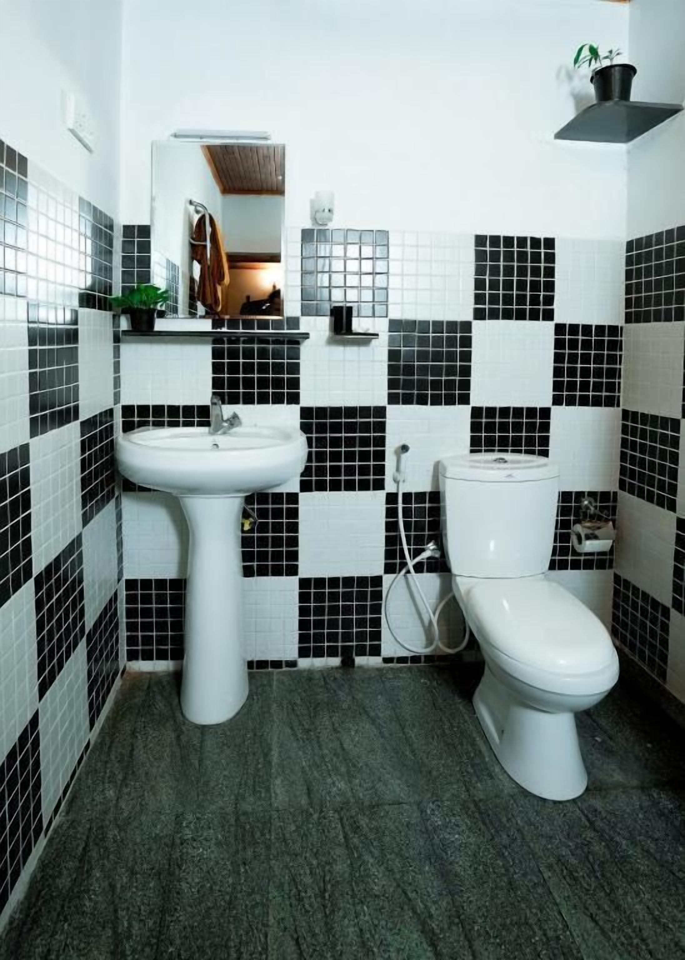 A bathroom with a sink, toilet, and a mirror. The walls are tiled in a black and white checkered pattern.