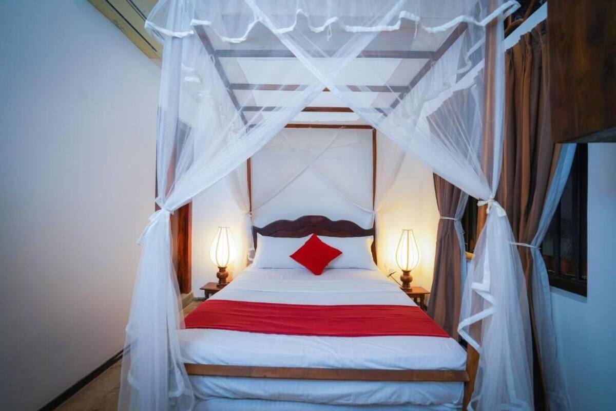 Un lit à baldaquin, deux lampes de chevet et un oreiller rouge.