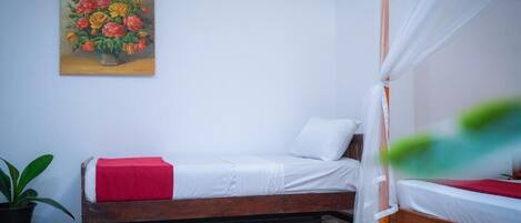 A bedroom with a wooden bed, white bedding, a red throw, a potted plant, and a painting of flowers on the wall.