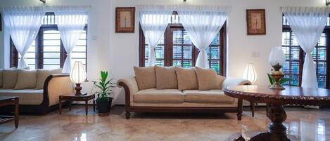 Un salón amplio con un sofá color beige, una mesa redonda de madera y una planta en maceta.