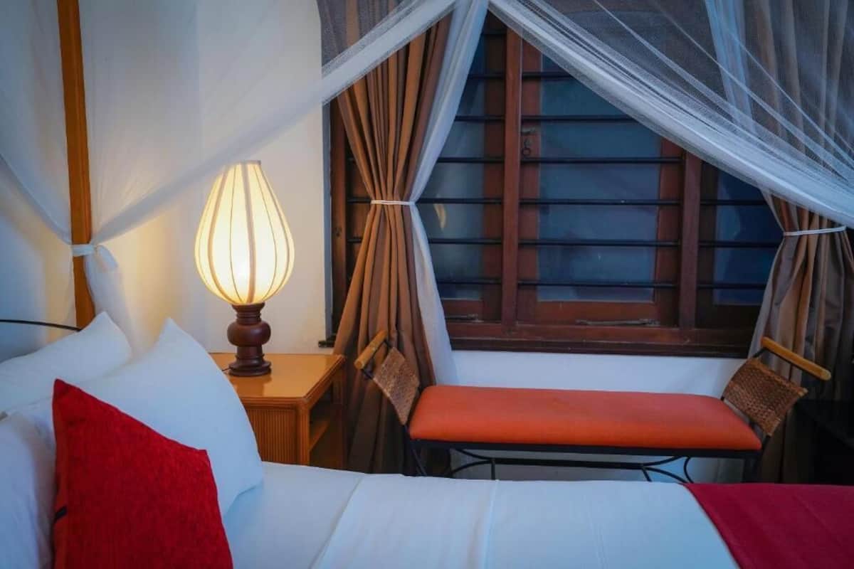 Une chambre à coucher avec un lit, une table de chevet avec une lampe, une chaise et une fenêtre avec des rideaux.