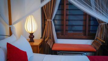 Ein Schlafzimmer mit einem Bett, einem Nachttisch mit Lampe, einem Sessel und einem Fenster mit Vorhängen.