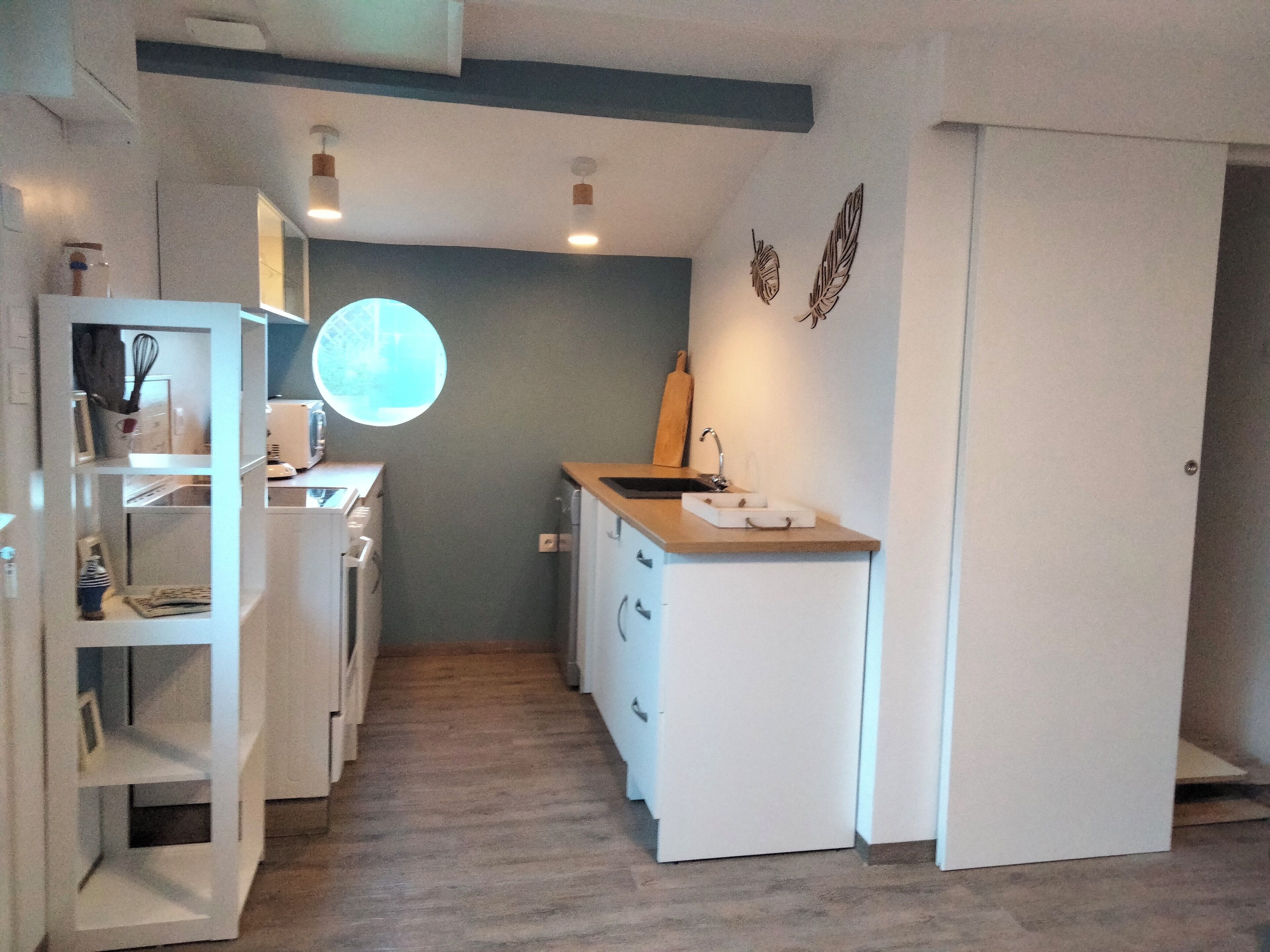 Kapea käytävä, jonka oikealla puolella on pieni keittiö, vasemmalla puolella valkoinen kaappi ja käytävän päässä ovi.