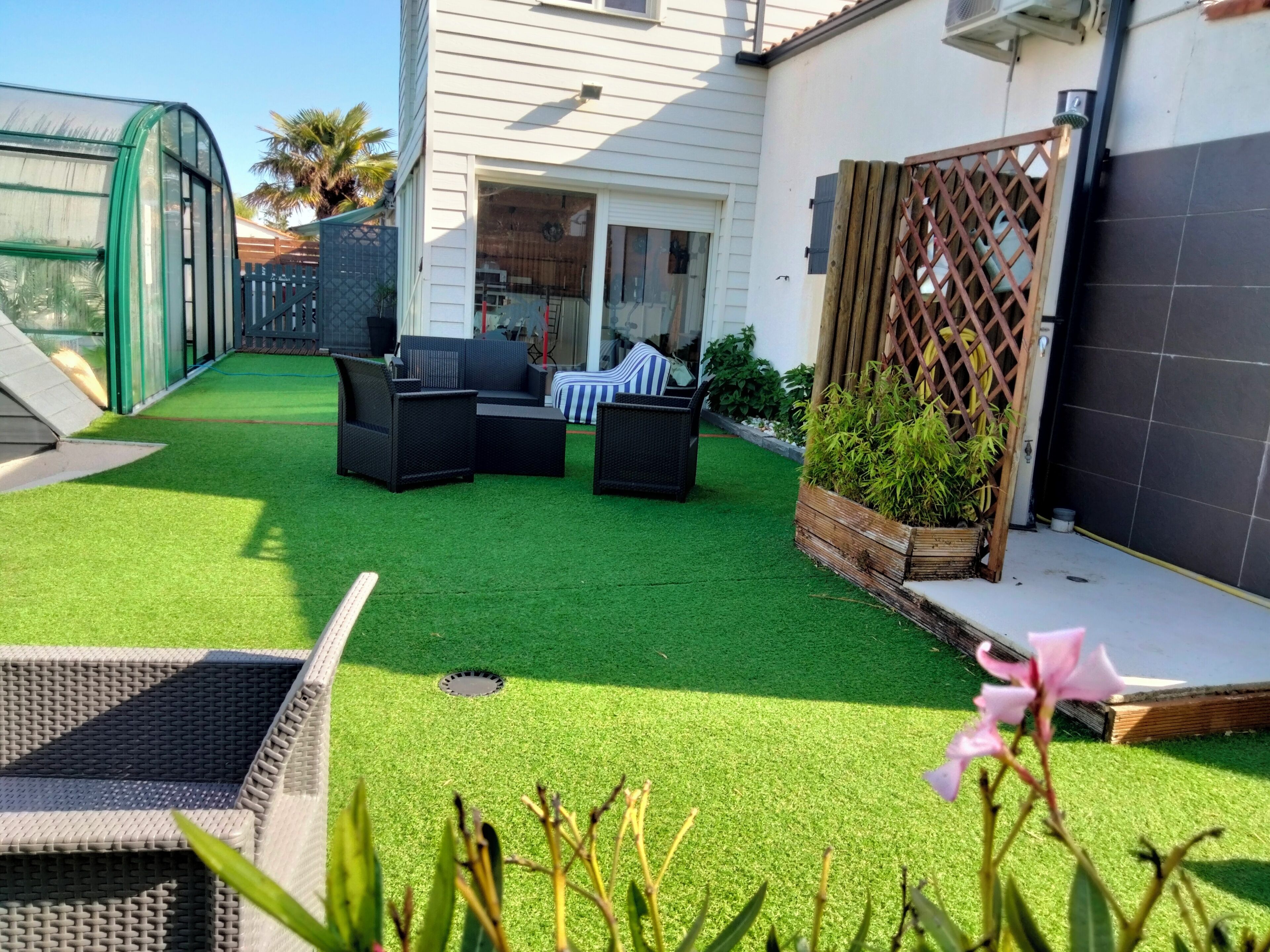 Un giardino pensile con erba sintetica, arredi da esterno e una struttura serra.