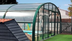 Estrutura de estufa com teto transparente, rodeada por relva sintética verde.