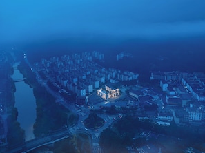 An aerial view of a cityscape at dusk with a prominent building with illuminated windows. - Zhangjiajie JIMO HOTEL (Zhangjiajie)