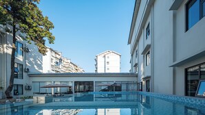 A swimming pool with a clear view of surrounding buildings, a covered seating area, and a staircase leading to an upper level. - Zhangjiajie JIMO HOTEL (Zhangjiajie)