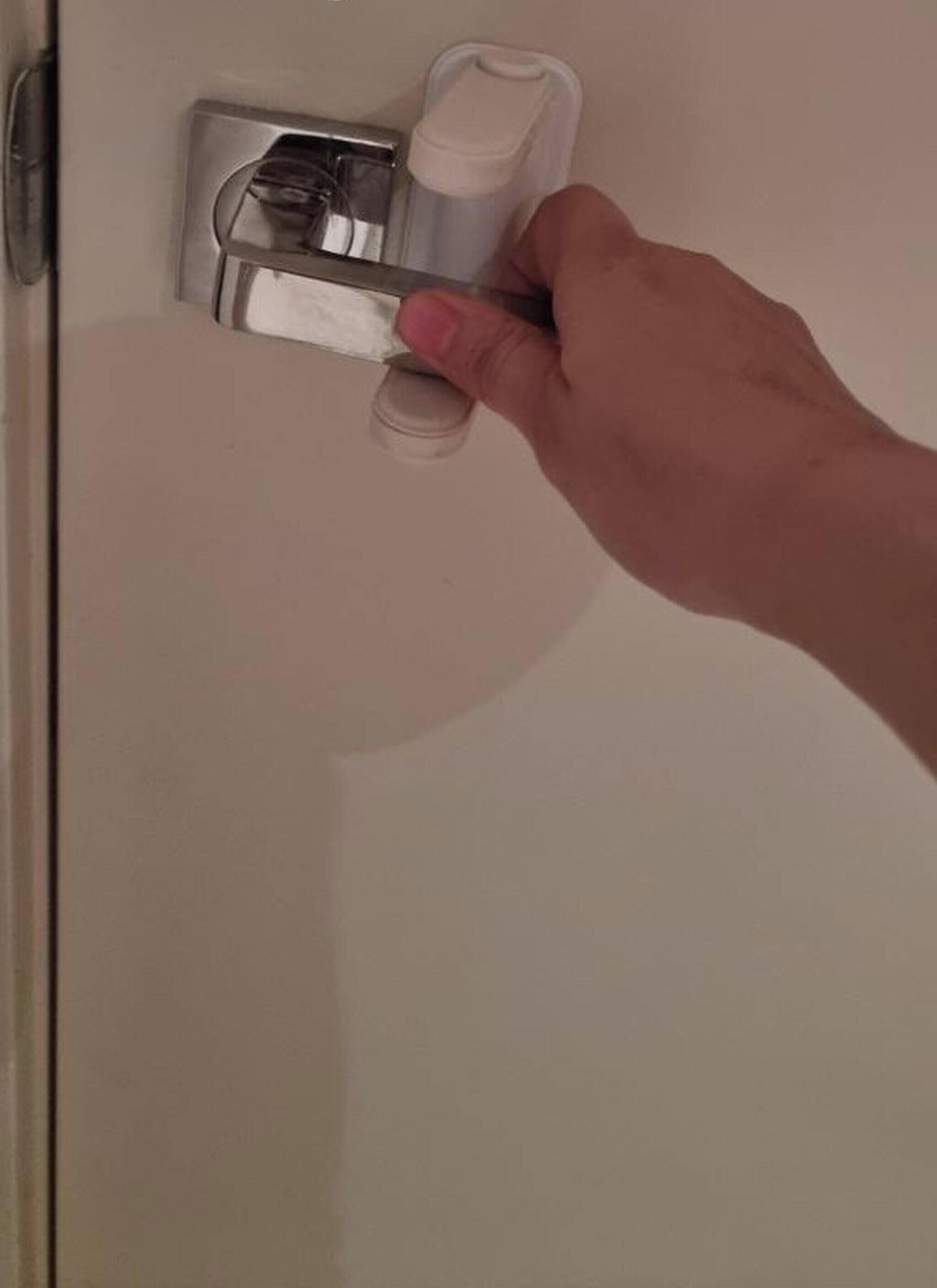 A hand holding a metallic object, possibly a tool, near a door handle.