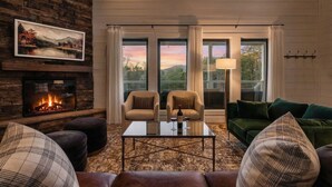 Una sala de estar acogedora con chimenea, dos sillones, un sofá verde y una mesa de centro de vidrio.