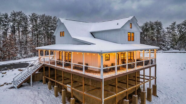 Una estructura de madera grande y de varios niveles con una terraza cubierta, rodeada de árboles cubiertos de nieve.