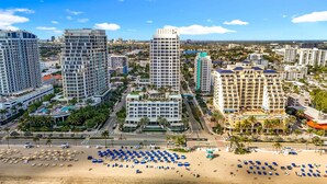 Eine Küstenstadt mit Hochhäusern, einem Strand mit Liegestühlen und einem klaren, blauen Himmel.