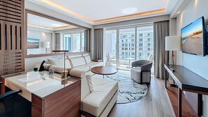Ein modernes Hotelzimmer mit einer Couch, einem Schreibtisch, einem Fernseher und einem Balkon mit Blick auf die Stadt.