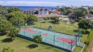 An outdoor basketball court surrounded by greenery and buildings, with a clear view of the ocean in the background. - Villa Ocean Dream 3BR Oasis and guesthouse (Sosúa)