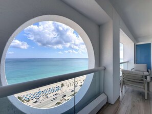 A balcony with a circular window overlooking a beach with umbrellas and a road. - Cozy Oasis in a Luxury Hotel w/Daily Cleaning (Fort Lauderdale)