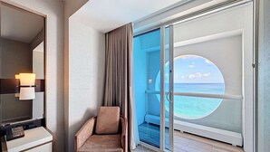 Habitación de hotel con un amplio ventanal corredizo que da a un balcón con vistas al océano.