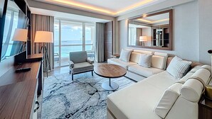 Camera d'albergo moderna con un ampio divano, una poltrona, un tavolino da caffè e una TV. Grande finestra con vista sull'oceano.