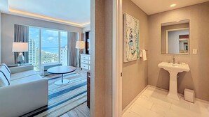 A hotel room with a large window offering a city view, a round table, a sofa, a desk, and a bathroom with a sink and mirror. - Cozy Oasis in a Luxury Hotel w/Daily Cleaning (Fort Lauderdale)